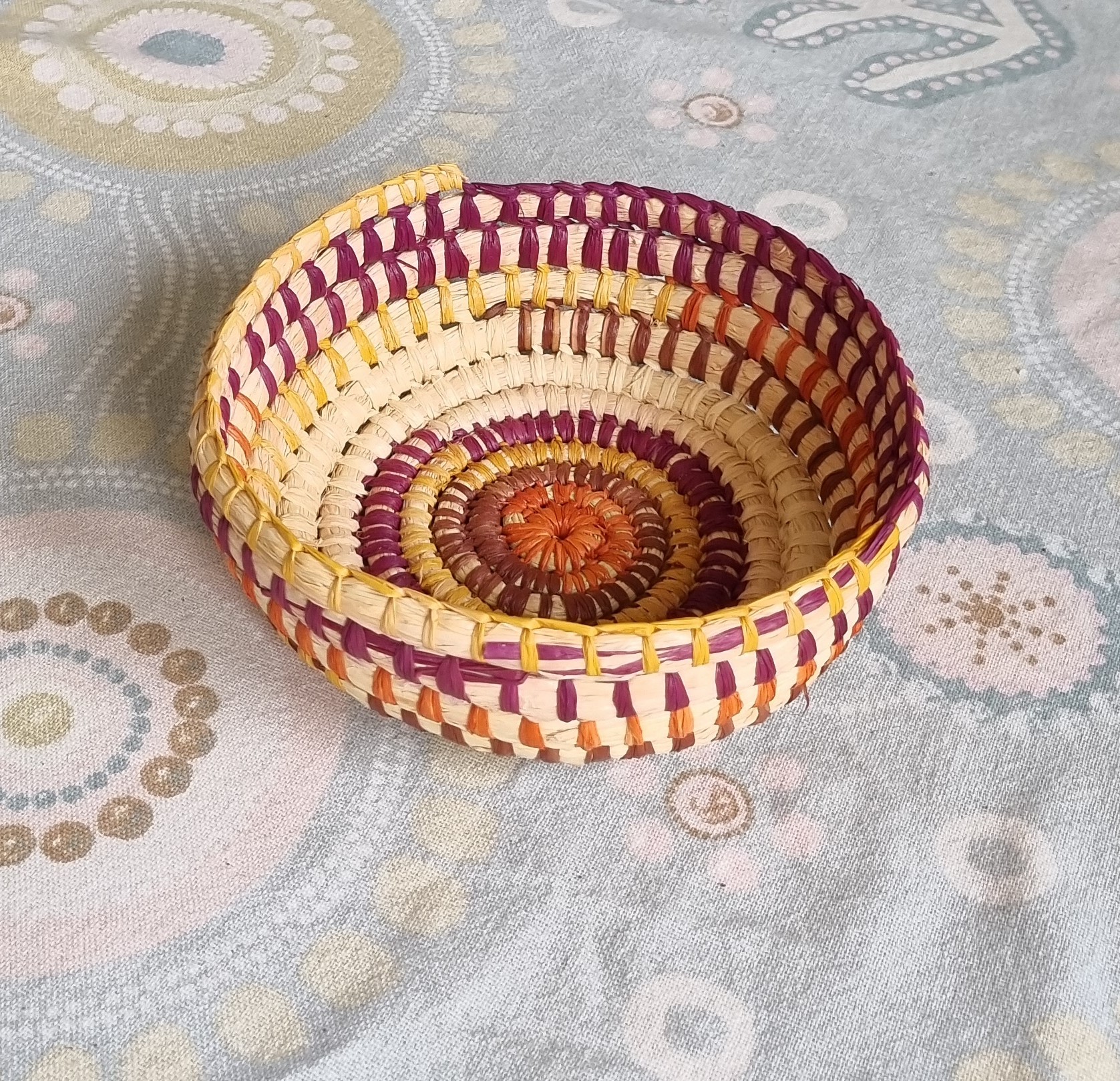 Hand woven small basket in natural raffia with purple, yellow, orange and brown colours by Palawa artist Belinda French